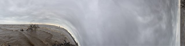 Un arbre arraché par la rivière en crue et rejeté en mer est revenu s’échouersur la plage. À l’horizon, on aperçoit le port industriel de Colombo. Il semble sombrer dans l’abîme : Ce n’est plus l’humain qui impacte la Terre, mais l’humain qui, en impactant ainsi la Terre, fait perdre le vivant, lui inclus, face au cosmos.